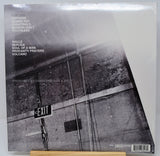 A vinyl record sleeve for the band Drowning Pool, featuring a black and white street scene with an EXIT sign. The tracklist is printed on the left side, and the record is sealed in shrink wrap, resting on a wooden surface.