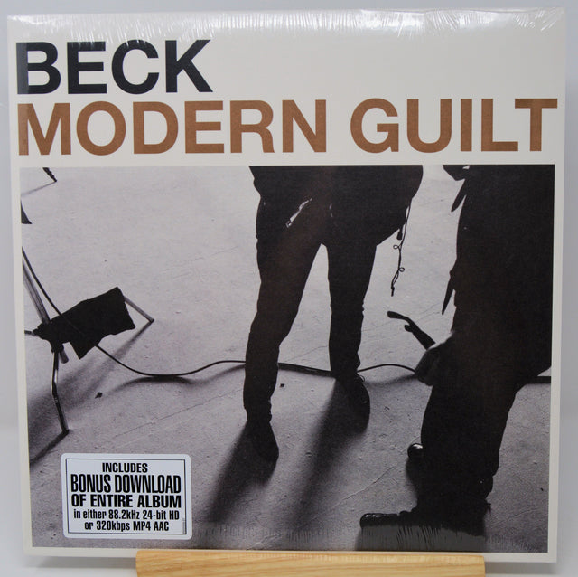 Beck's 'Modern Guit' vinyl record cover, sealed in plastic and displayed on a wooden stand. The cover features a black and white photograph of musicians with the title in bold brown and black lettering.
