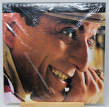 A square printed artwork or poster showing a close-up portrait of a smiling man wearing a hat, photographed wrapped in clear plastic with visible creases. The top edge has faint text reading 'ORIGINAL MOTHER-DEADLY DOOMING.
