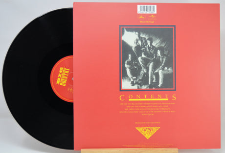 A vinyl record partially pulled from its red sleeve, showing the black record, orange center label, and the red cover with a black-and-white band photo and the word 'CONTENTS'.