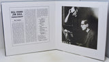 An open book or magazine spread showing a printed article on the left page with the headline 'Bill Evans Jim Hall Undercurrent' and a black-and-white photograph on the right page depicting two men seated at a piano.