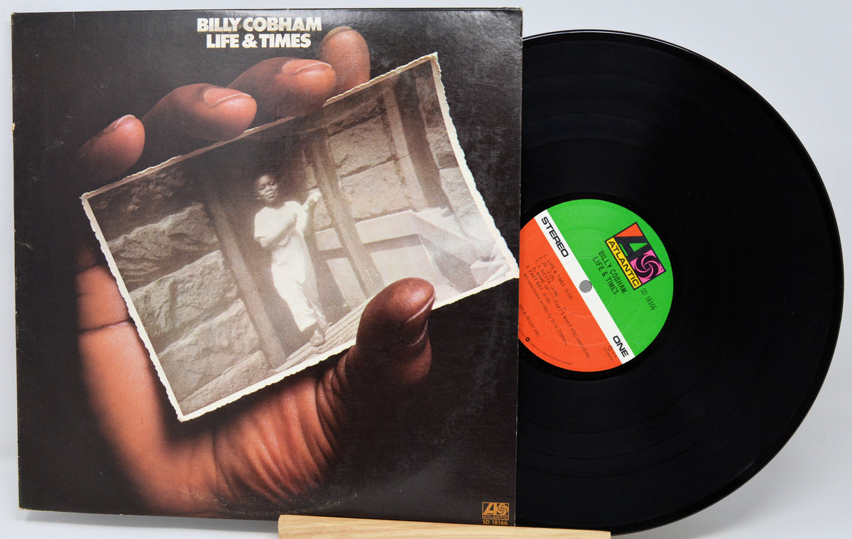 Billy Cobham's 'Life & Times' vinyl record LP with its cover jacket and the black vinyl disc partially pulled out, displayed on a light background.