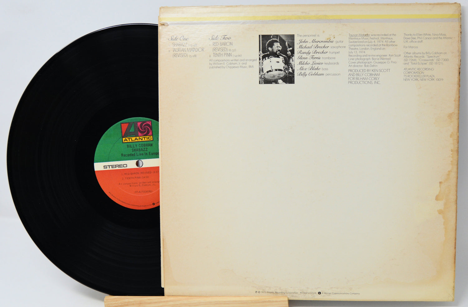 A vintage vinyl record partially pulled from its cream-colored paper sleeve, showing the black record, a green and orange center label, and printed tracklist text on the cover.