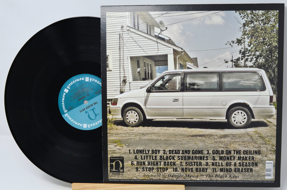 A vinyl record partially pulled from its album jacket, showing the black record and the printed cover art for Starship's 'The Black Star'. The cover features a white van parked in front of a house, with the tracklist printed at the bottom.