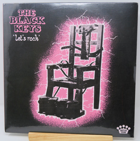 Album cover for the black keys lets rock with a picture of an electric chair on a pink background