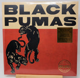 Black Pumas 'Greatest Hits Deluxe Edition' vinyl record album cover, featuring two black panthers on a red background with a beige header and black text. A gold sticker on the right details the 2 LP set, and a round '40th Year Deluxe Edition' seal is visible at the bottom right.