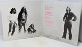 An open vinyl record sleeve or booklet showing printed cover art with black-and-white band photos and pink tracklist text on a light background.