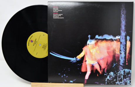 Vinyl record album with the black LP partially pulled from the sleeve, showing the cover art of a figure in a red coat holding a sword in a dark scene. The record label is yellow and the sleeve includes printed track listing text.