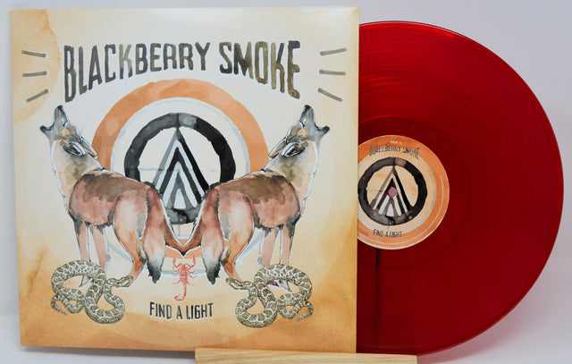 Blackberry Smoke vinyl record album with the illustrated cover jacket in front and a translucent red vinyl record partially visible behind it on a light gray background.