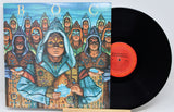A vinyl record album with its illustrated cover jacket shown beside the black record. The cover art features a stylized group of hooded figures in ornate robes against a blue sky, with the title text 'Blue Oyster Cult' and 'The Holy Oyster' visible.