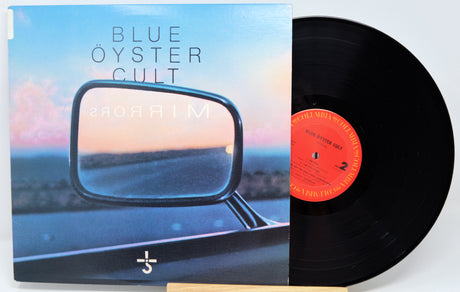 Blue Öyster Cult 'Mirrors' vinyl record with the album cover in front and the black LP partially pulled out, showing the orange center label.