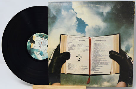 Vinyl record with a cover featuring an open book held by hands against a cloudy sky.