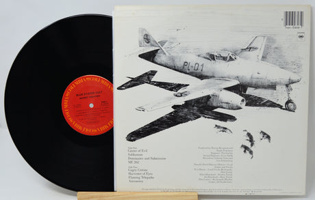 A vinyl record partially slid out of its printed album cover, showing a black record with a red-orange center label beside the back cover featuring black-and-white illustrations of military aircraft.