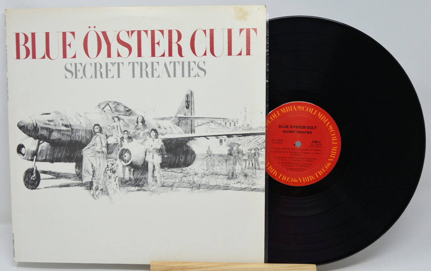 Blue Oyster Cult's 'Secret Treaties' vinyl record album, showing the illustrated white cover with red title text and a black LP partially pulled out, with a red center label.