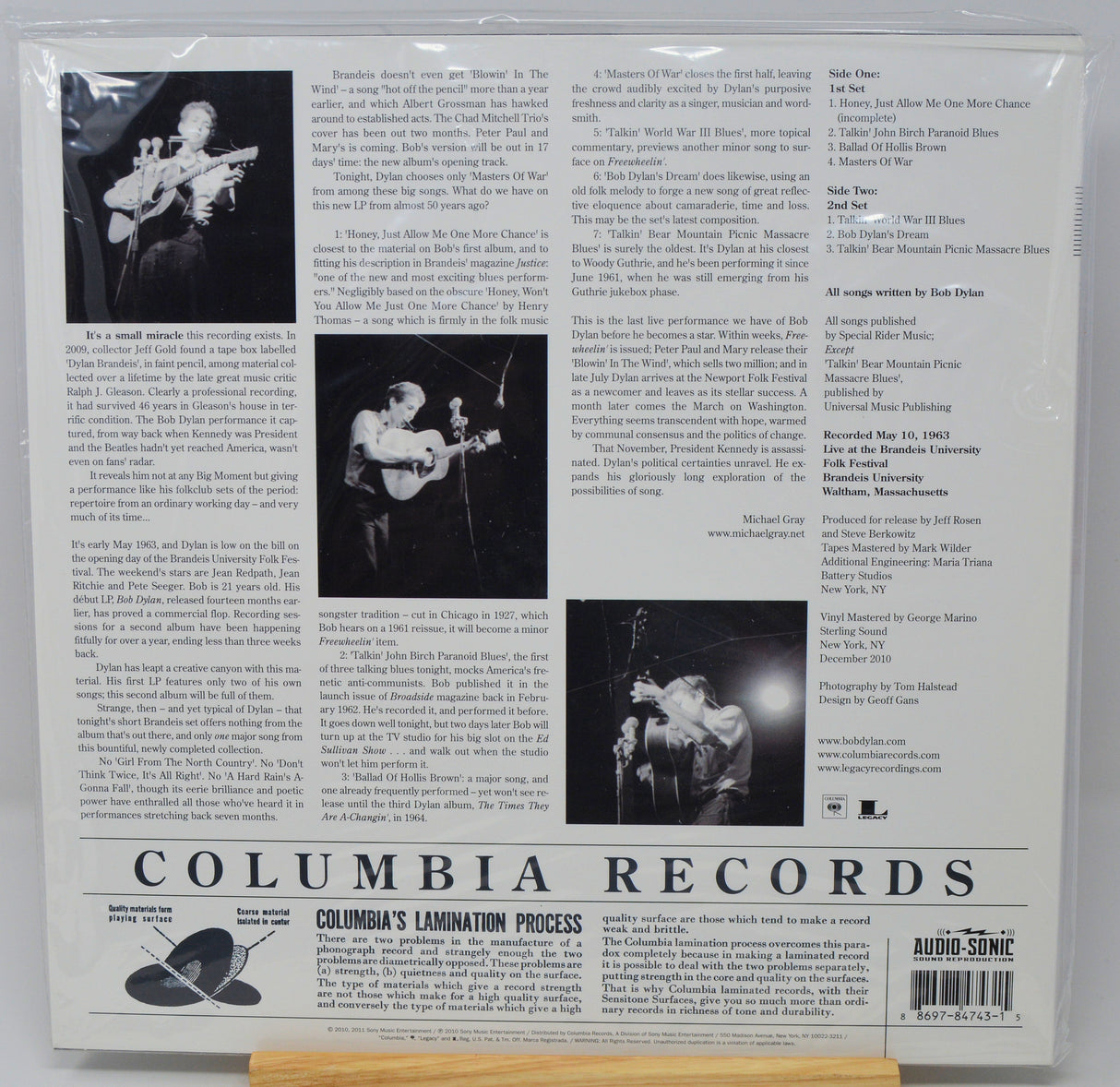 The back cover of a Columbia Lamination Records music release, featuring track listings, biographical text, and black-and-white photos of a performer on stage, sealed in a plastic sleeve.