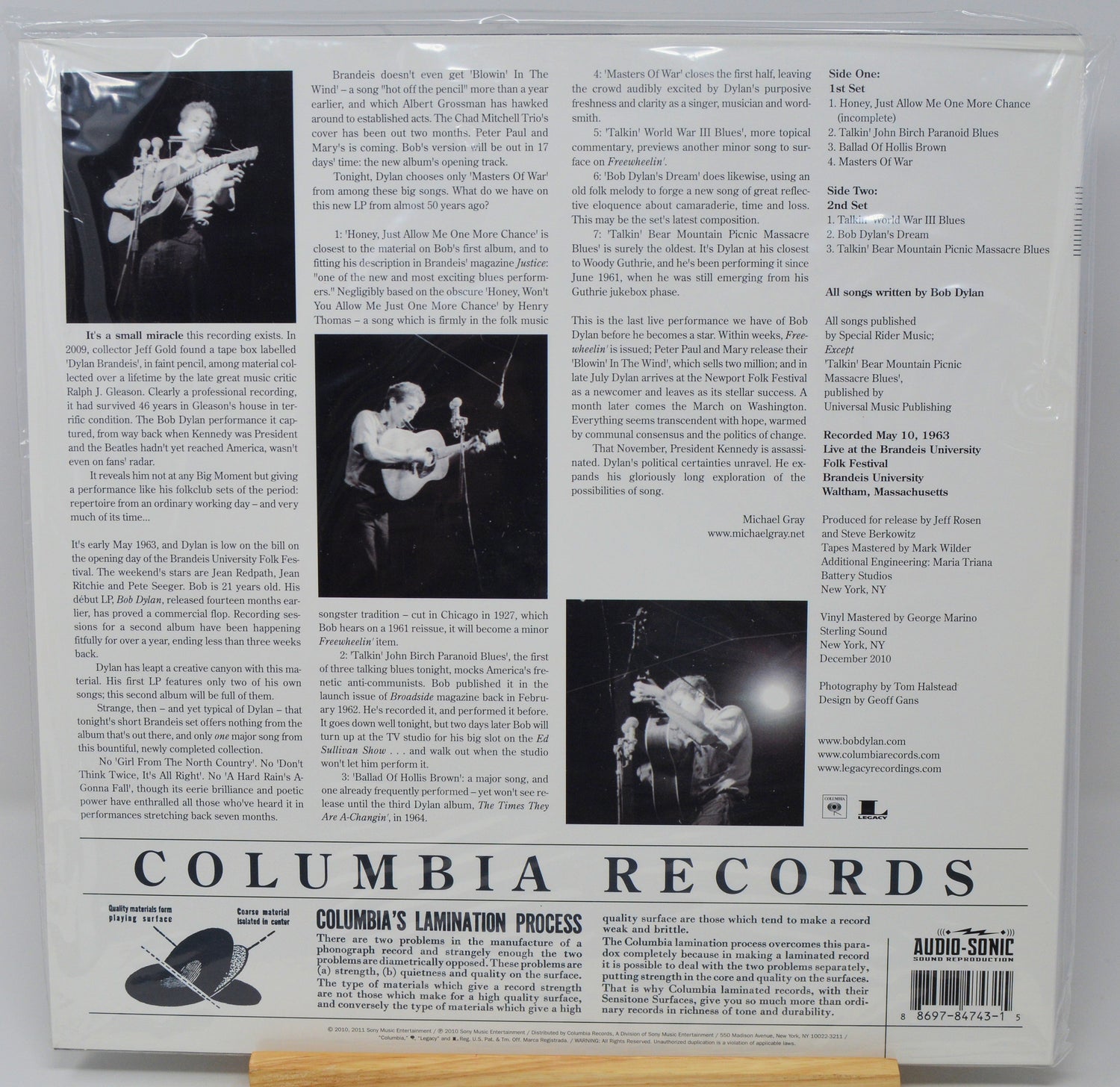 The back cover of a Columbia Lamination Records music release, featuring track listings, biographical text, and black-and-white photos of a performer on stage, sealed in a plastic sleeve.