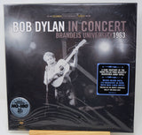 Bob Dylan 'In Concert' Brandeis University 1963 vinyl record album cover, showing a black-and-white concert scene with a guitar and microphone, plus a blue sticker and a gold-plated LP badge.