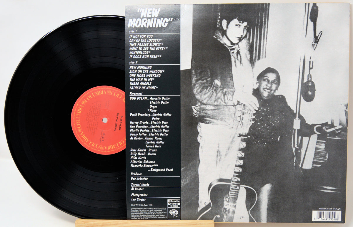 Vinyl record album 'New Morning' with the black LP partially pulled from the sleeve, showing the tracklist on the back of the cover and a black-and-white photo of two people holding guitars.