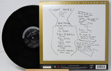 Bob Dylan's 'Planet Waves' vinyl record album shown with the black LP partially pulled from the gatefold cover, which is signed and features tracklist handwriting on a white background.