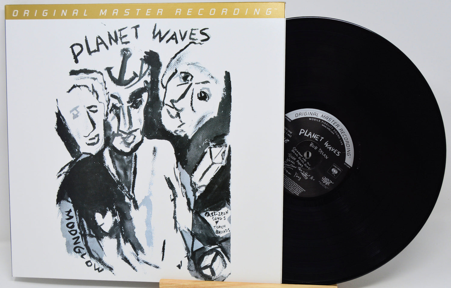 A vinyl record album shown with its illustrated outer sleeve and the black record partially pulled out. The sleeve reads 'PLANET WAVES' and 'ORIGINAL MASTER RECORDING.