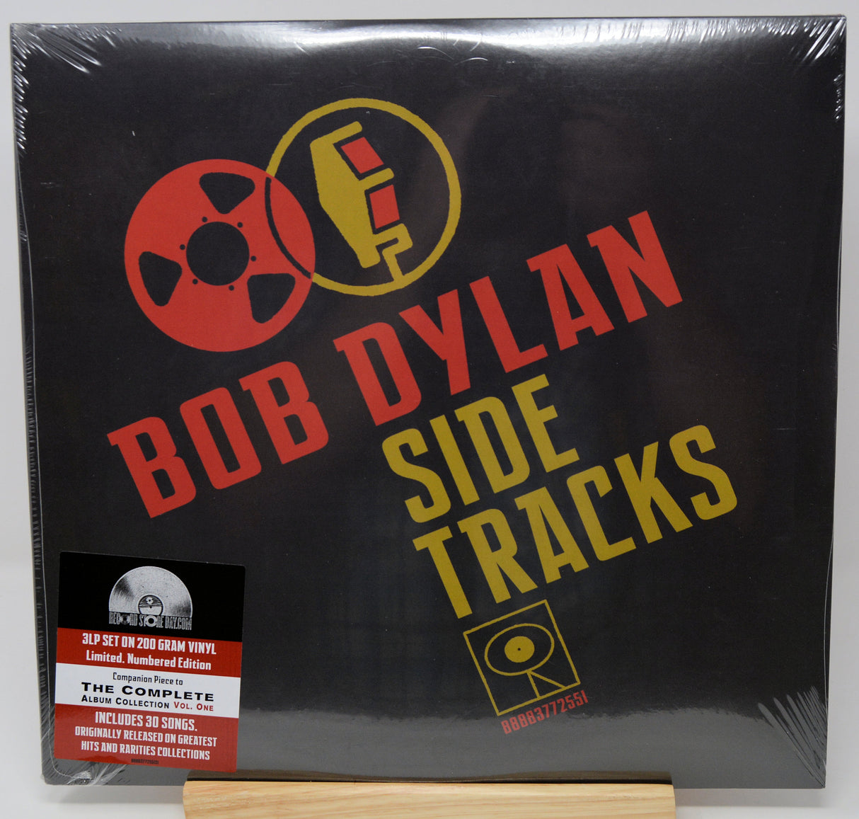 Bob Dylan 'Side Tracks' 12-inch vinyl record cover, sealed in plastic shrink wrap and displayed on a small wooden stand. The cover is black with bold red and yellow text and graphics, and a JYP Records sticker is visible in the lower-left corner.