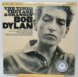Bob Dylan's 'The Times They Are A-Changin'' original master recording vinyl LP on Monuhal, sealed in a protective plastic sleeve. The cover features a black and white portrait of Bob Dylan with bold black text on a warm beige background, and a silver 'Limited Edition of 2000' sticker on the bottom right.