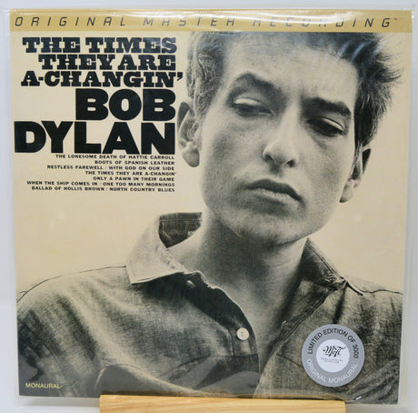 Bob Dylan's 'The Times They Are A-Changin'' original master recording vinyl LP on Monuhal, sealed in a protective plastic sleeve. The cover features a black and white portrait of Bob Dylan with bold black text on a warm beige background, and a silver 'Limited Edition of 2000' sticker on the bottom right.