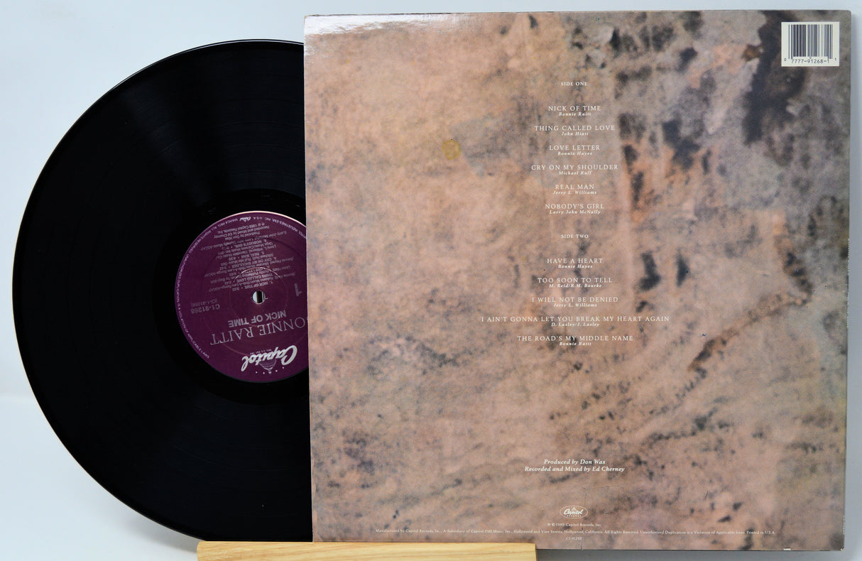 A vinyl record partially pulled from its back cover sleeve, showing the black record with a purple center label and the marbled beige-and-brown album artwork behind it.