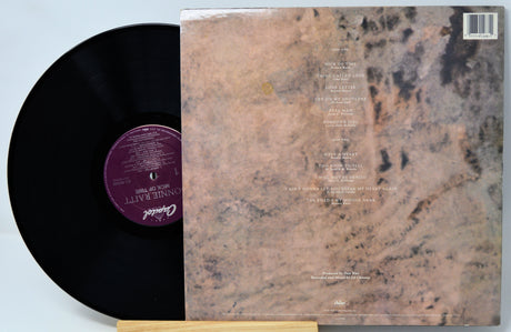 A vinyl record partially pulled from its back cover sleeve, showing the black record with a purple center label and the marbled beige-and-brown album artwork behind it.