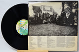 A vinyl record partially pulled from its sleeve, showing the black record on the left and the back cover of the album on the right with a black-and-white group photograph and printed track text on a cream background.