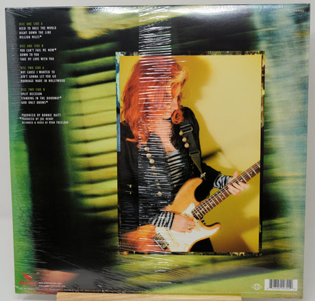 The back cover of a vinyl record album wrapped in protective plastic, featuring a green and black abstract background with track listings on the left and a central inset photo of a woman playing an electric guitar.