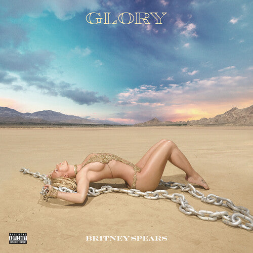 Britney Spears posing in a gold outfit with chains on a desert landscape for the Glory album cover