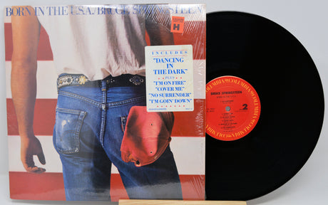 Vinyl record with cover featuring a person in jeans and a red object, on a light gray background.