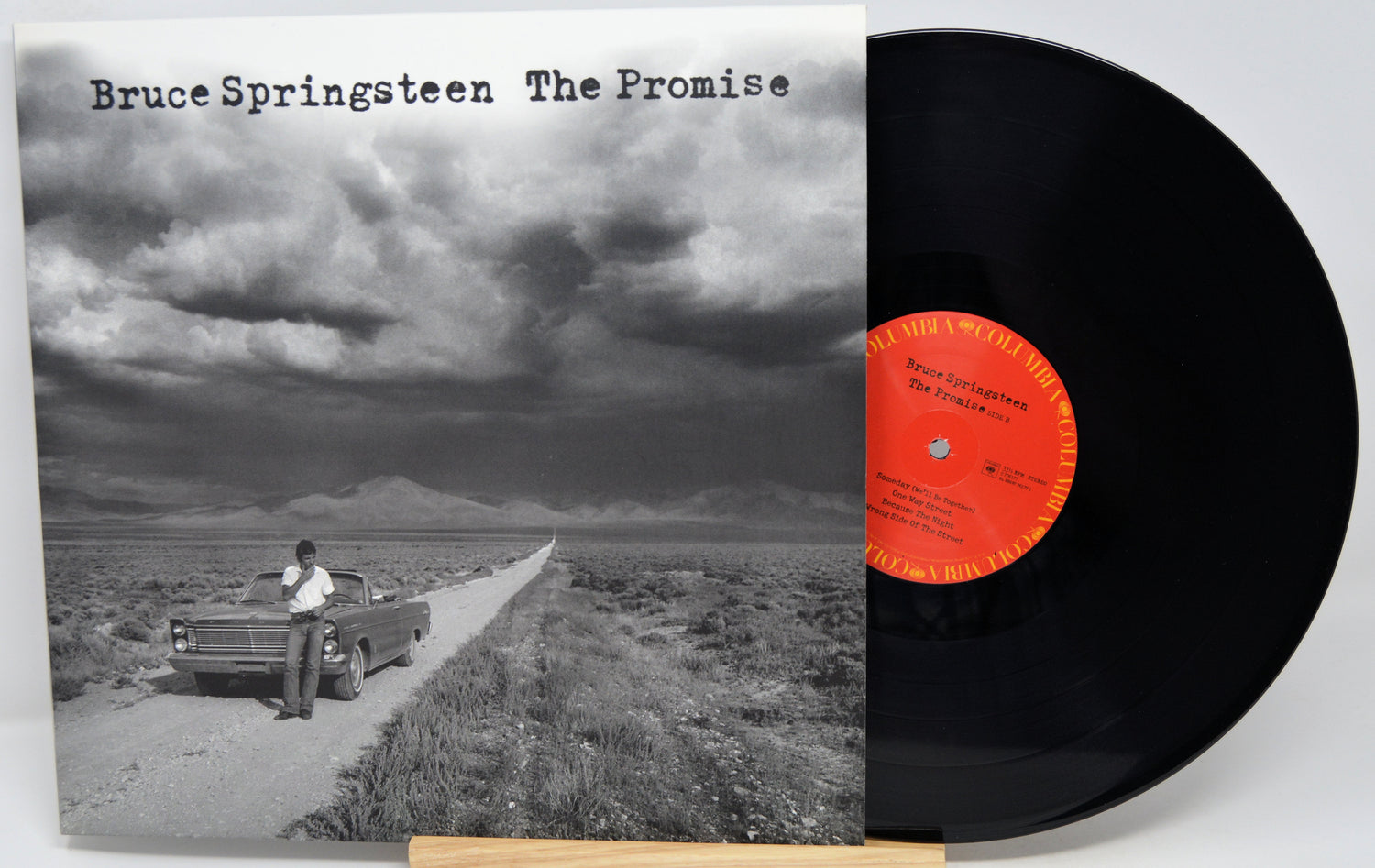 Bruce Springsteen 'The Promise' vinyl record LP with its album cover in front of the black record, photographed on a light gray background.