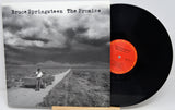 Bruce Springsteen 'The Promise' vinyl record LP with its album cover in front of the black record, photographed on a light gray background.