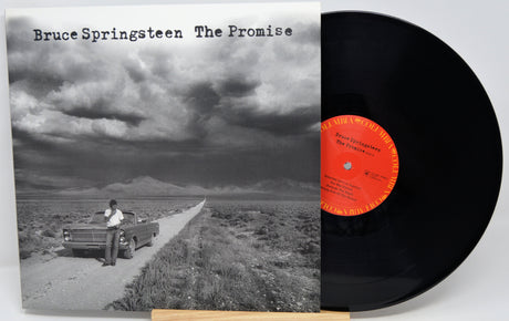 Bruce Springsteen 'The Promise' vinyl record LP with its album cover in front of the black record, photographed on a light gray background.