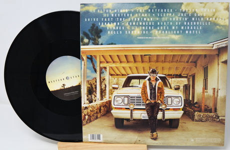 A vinyl record partially pulled from its sleeve, showing the black disc on the left and the album cover on the right. The cover features a man standing in front of a white car under a blue sky, with the text 'Hitch Hike' and tracklist visible at the top.