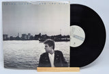 Vinyl record with a cover featuring a person by a waterfront, on a light gray background.