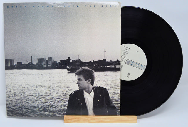 Vinyl record with a cover featuring a person by a waterfront, on a light gray background.