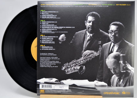 A vinyl record partially pulled from its back cover sleeve, showing the black record and a black-and-white album photo with track listing text. The sleeve features two men in suits and a saxophone, and the record label shows Creative Records branding.