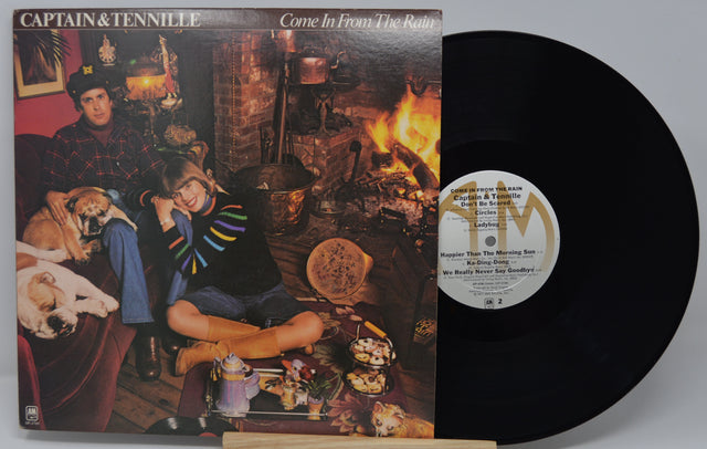 Vinyl record with cover featuring two people and a dog in a cozy room setting.