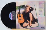 Vinyl record with a cover featuring a woman and guitar, on a light gray background.