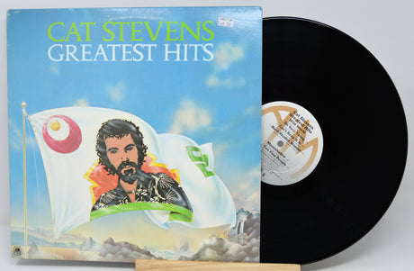 Cat Stevens Greatest Hits vinyl record album with the illustrated cover on the left and the black LP record partially pulled out on the right, photographed against a light gray background.