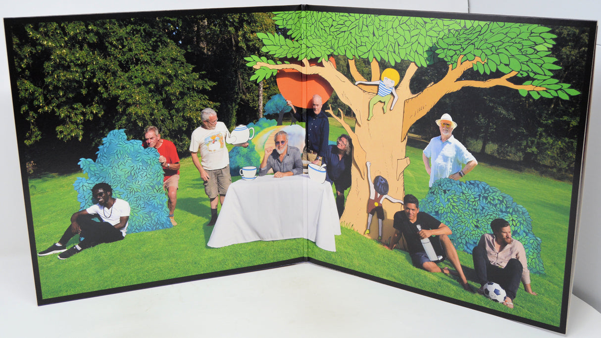 A large pop-art style poster or print showing multiple people gathered outdoors around a table under a tree, with a stylized cartoon-like tree and grassy background. The print is photographed standing against a plain light background.