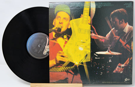 A vinyl record partially pulled from its album cover, showing a black record on the left and the printed cover art on the right. The cover features a split photo of a musician playing guitar and singing, with a bright yellow light flare effect across the center.