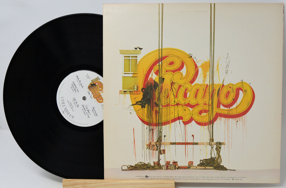 A vinyl record partially pulled from its sleeve, showing the black record on the left and the illustrated album cover on the right. The sleeve features a large yellow and red graffiti-style logo reading 'Chicago' with a cityscape illustration below.