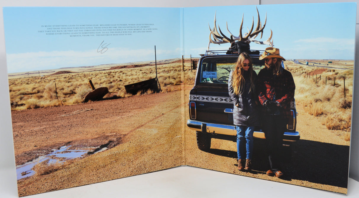 Two people standing next to a truck with deer antlers on a desert landscape