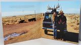 Two people standing next to a truck with deer antlers on a desert landscape