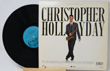A vinyl record partially pulled from its album cover, featuring Christopher Holaday. The cover has a cream background with bold black text and an illustration of Christopher Holaday in a suit holding a saxophone.