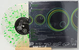 A vinyl record album shown with the back cover and part of the translucent record. The record is clear with bright green paint splatter, and the cover is black with green and yellow circular graphics and track listing text.